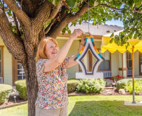 Senior Woman Hanging Decorative Art in Outdoor Courtyard at Assisted Living Facility