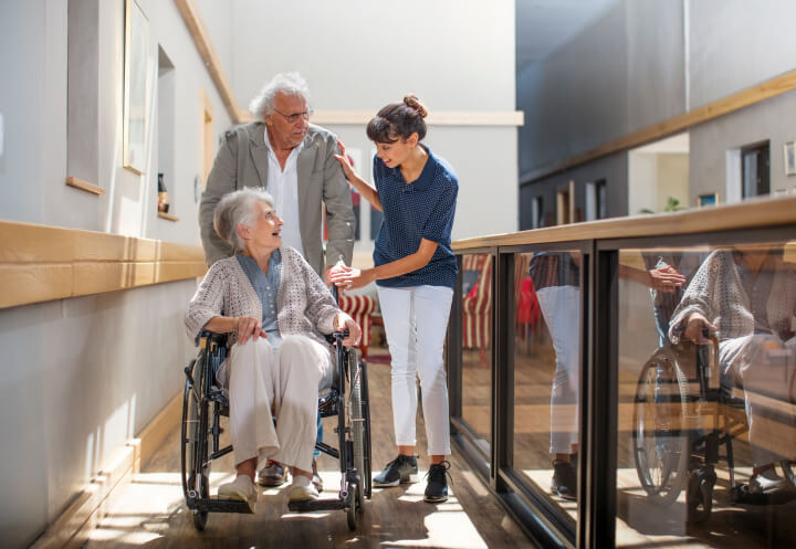 Female Nurse Assisting a Senior Couple Through the Hallway of a Memory Care Facility
